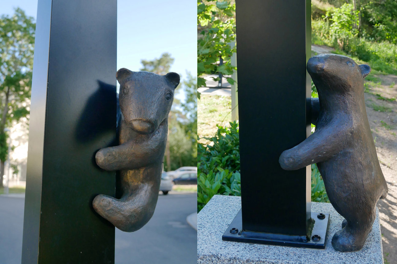 Två bronsbjörnsskulpturer som klamrar sig om en svart pelare utomhus.