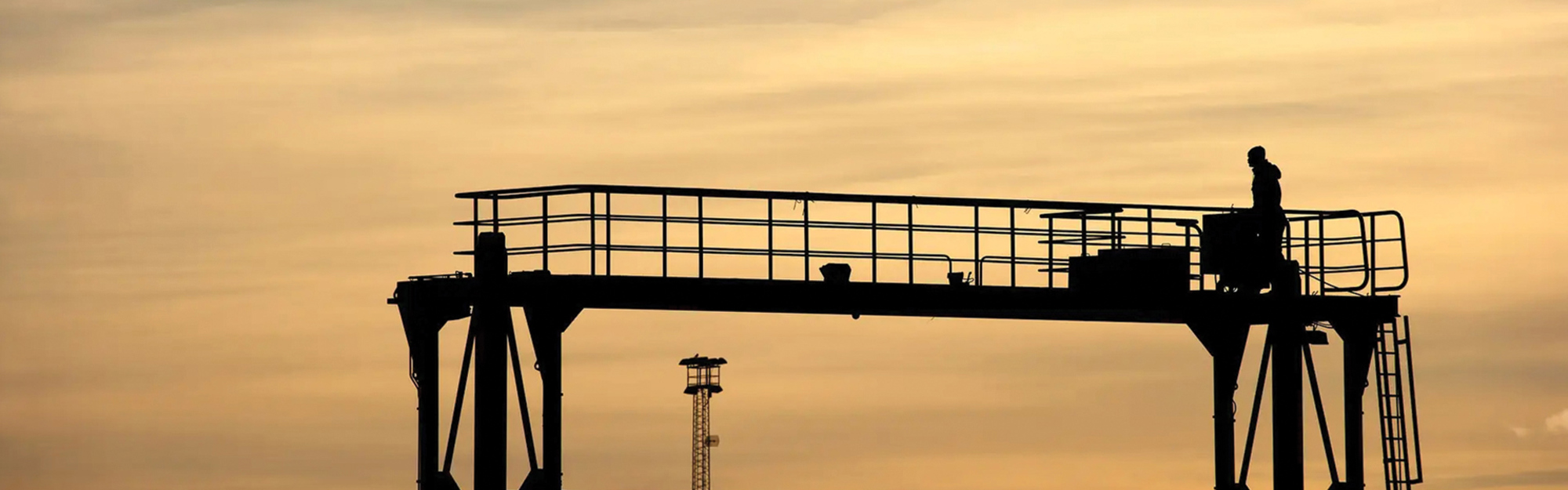 Silhuett av en person på en industriell plattform mot en solnedgångshimmel.