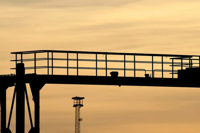 Silhuett av en person på en industriell plattform mot en solnedgångshimmel.