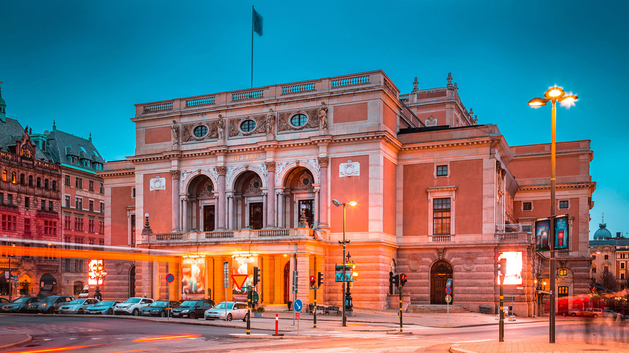 Stor historisk byggnad med arkader och gatubelysning vid kvällstid.	