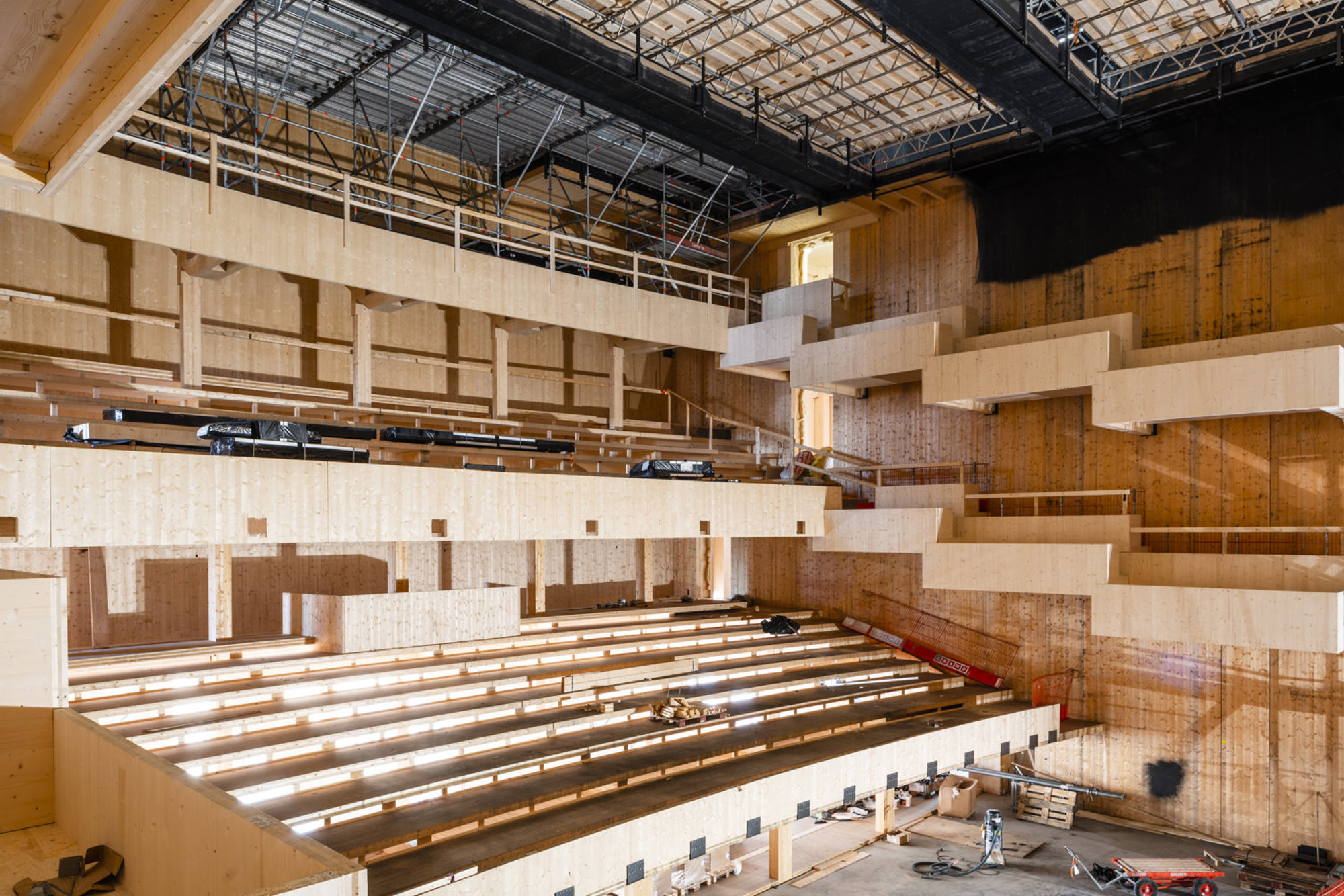 Inredningen av en byggnad under konstruktion med träkonstruktioner, ställningar och tomma läktarplatser.