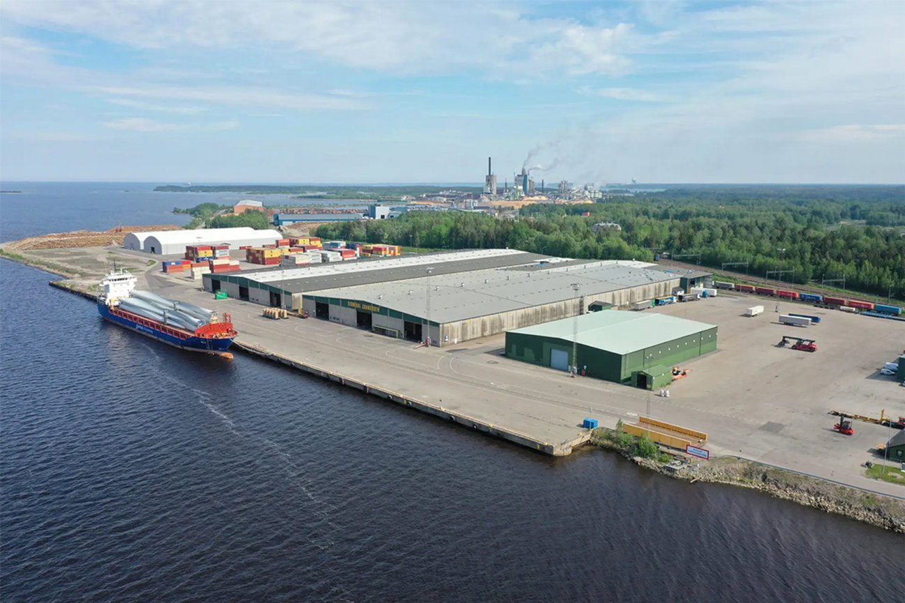 Industrihamn med fartyg, containrar och byggnader vid vatten.