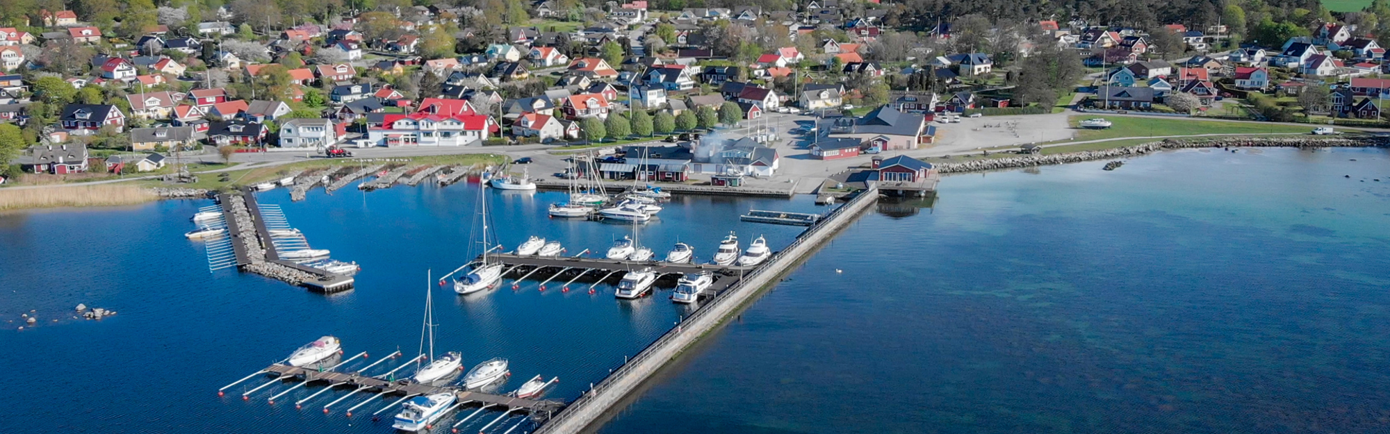 Flygfoto av en hamn med båtar, bryggor och hus vid vattnet.