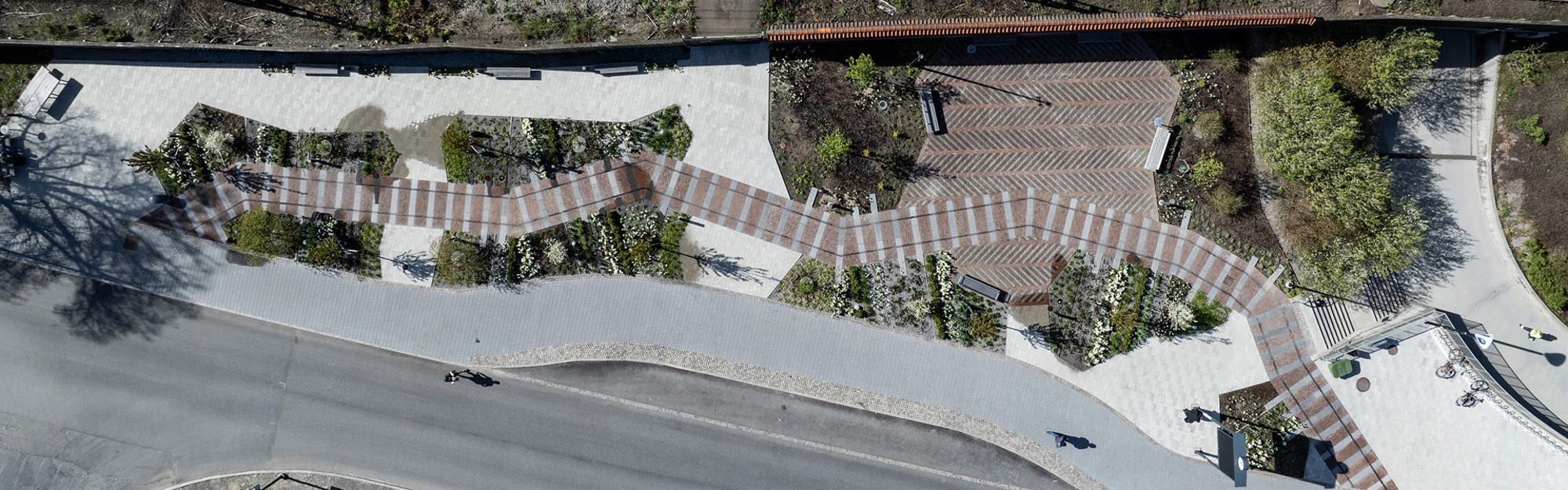 Luftbild av en utomhusplats med mönstrade stigbanor, växter och en väg.