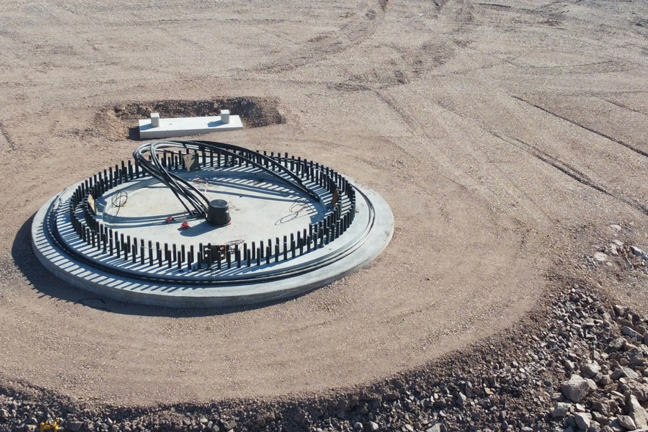 Cirkulär betongstruktur med rör på sandig och stenig markyta.