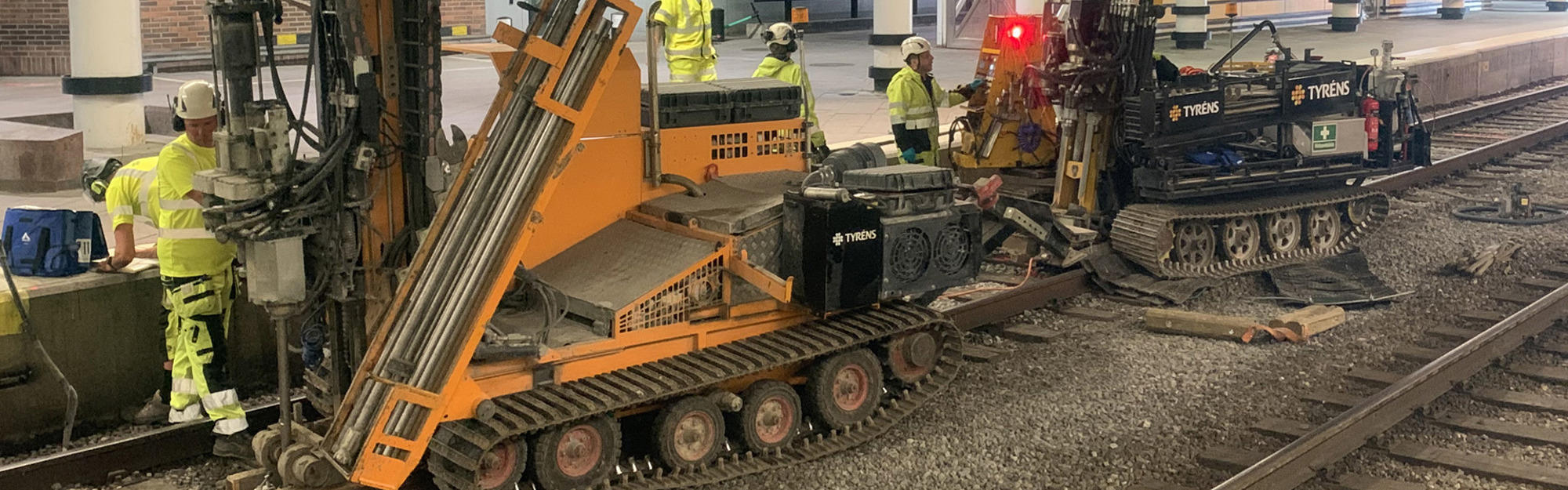 Järnvägsunderhåll med maskiner och arbetare i gula säkerhetsvästar på spåren.