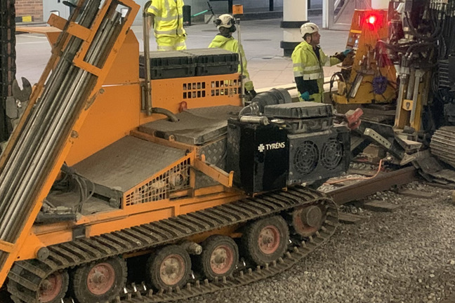 Järnvägsunderhåll med maskiner och arbetare i gula säkerhetsvästar på spåren.