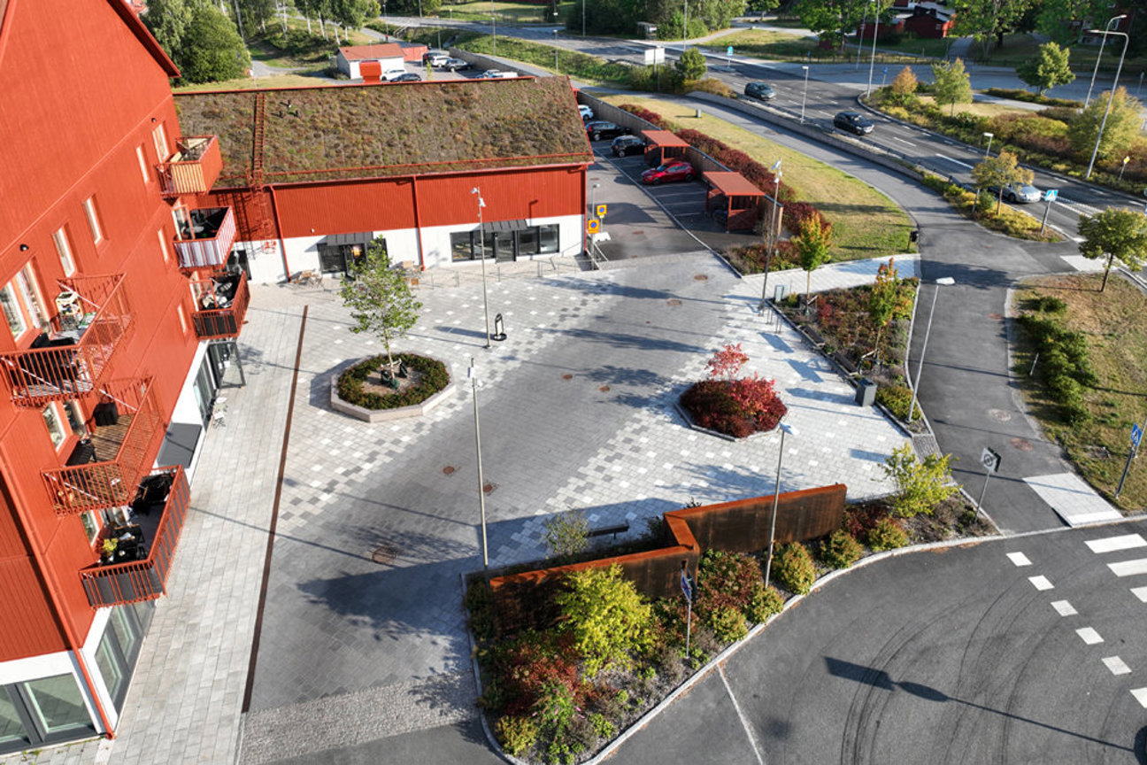 Röd byggnad med grönt tak, parkeringsplats och vägar omgiven av träd och buskar.