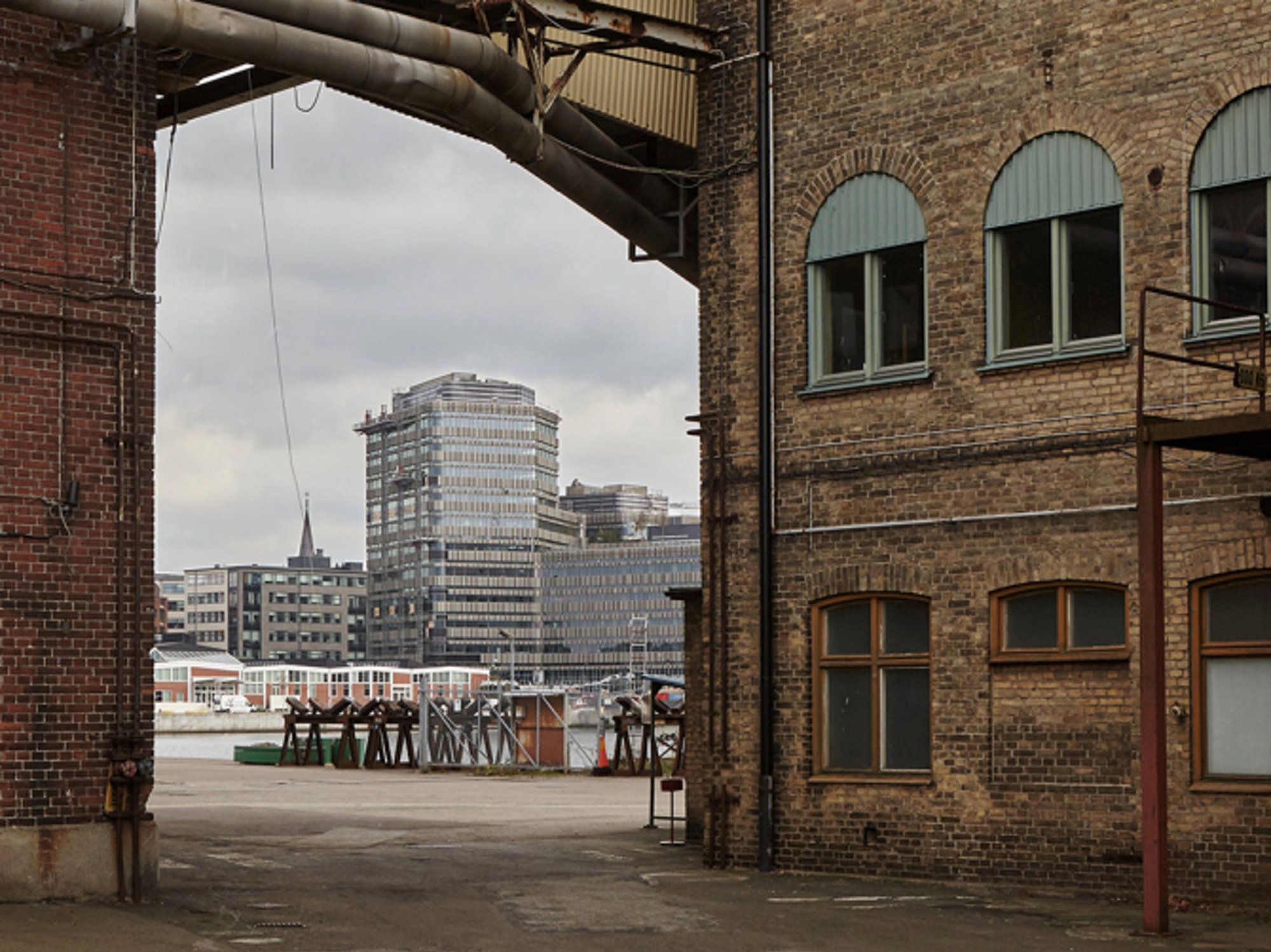 Tegelbyggnader med båge och stadslandskap i bakgrunden under molnigt väder.
