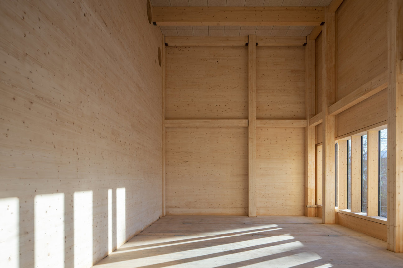 Tomt rum med träväggar, bjälkar och fönster som släpper in solljus.